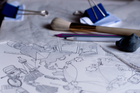 The picture shows a close up of my drawing table with a piece of paper and several pencils, erasers and tools. The part of the pencil drawing that is in focus shows 3 different globe-style views of the planet earth with various technical artifacts arranged around them.